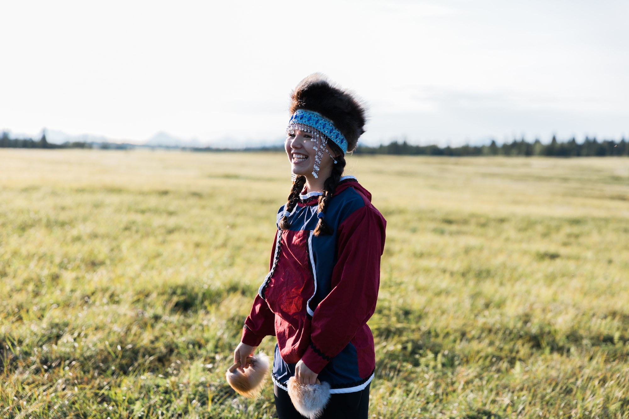 Choggiung Shareholder and descendent stands in a field with traditional Alaska Native clothing on during sunset.