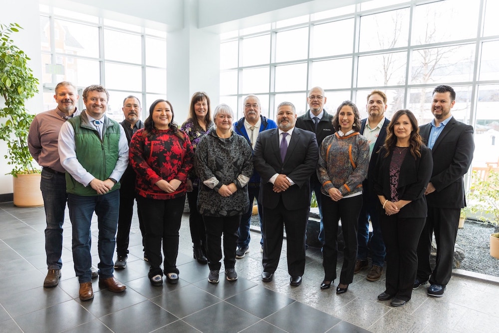 Choggiung Board of Directors and Executive Leadership posing for a photo in a bright lobby with large windows and a potted plant, exhibiting a range of business casual attire and approachable expressions.